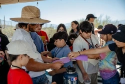 Children gather around an educator who is passing out supplies.