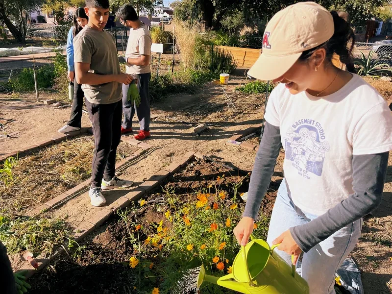 A group of people working on a garden plot and holding tools like watering cans.