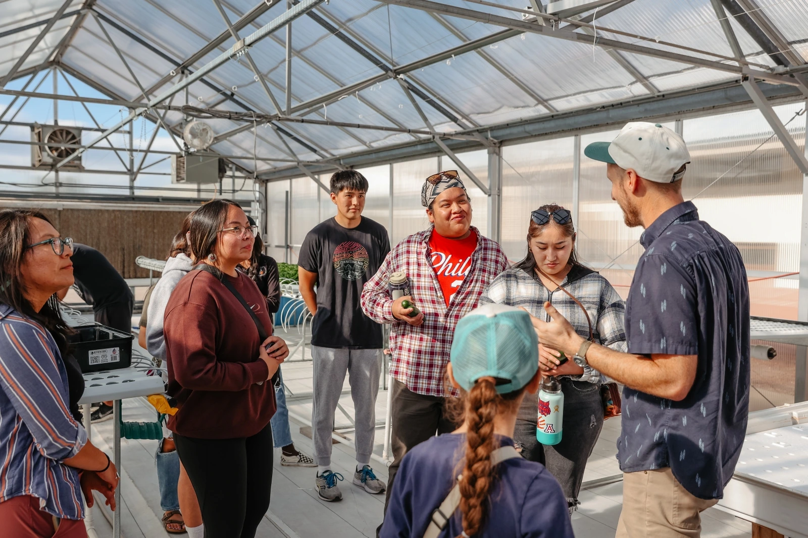 A group of people are standing together talking to one another inside of a greenhouse.