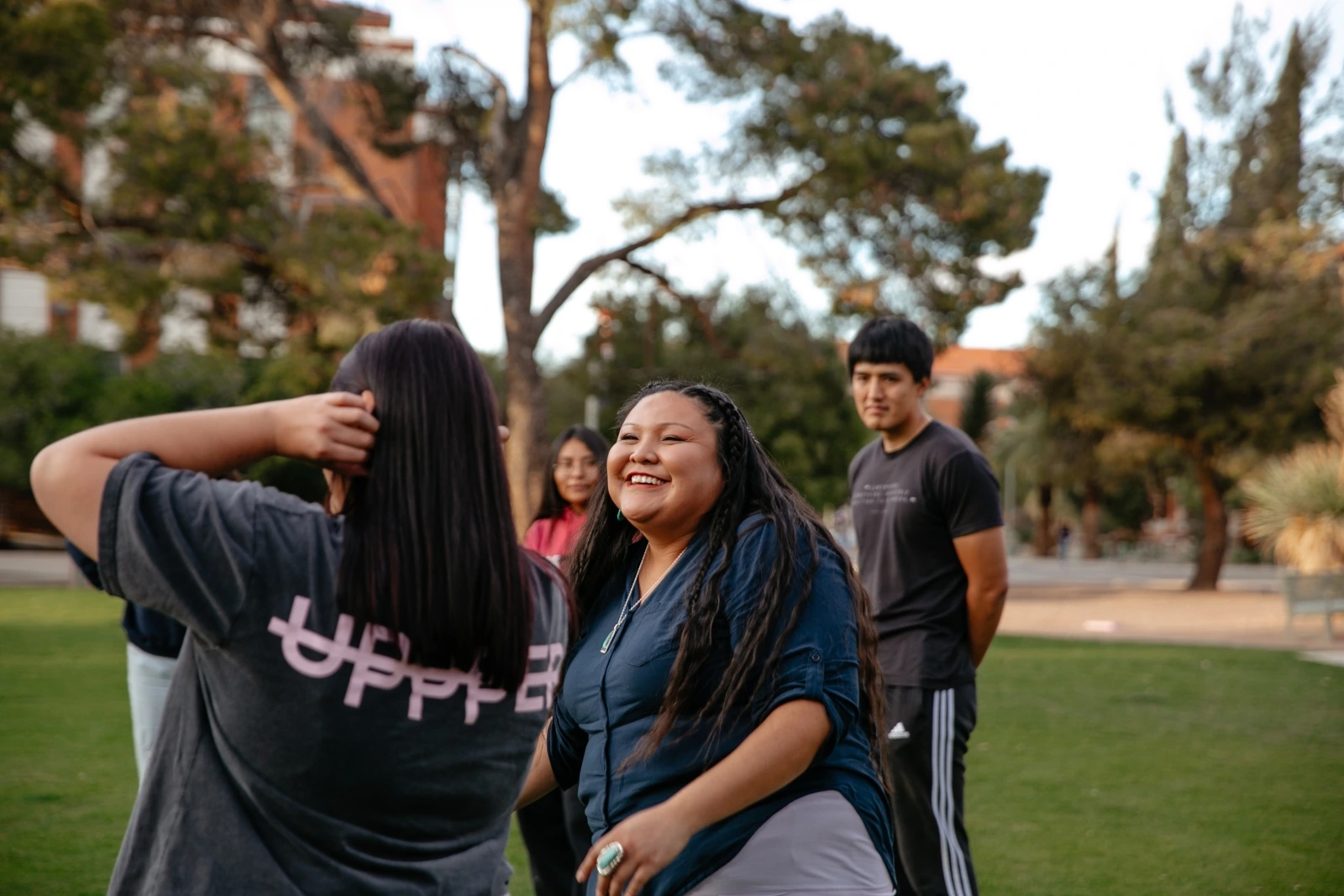 Three people standing next to each other talking. They are standing on a grass field.