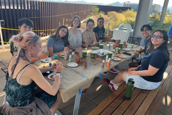 Students and staff sit around a table painting pots.
