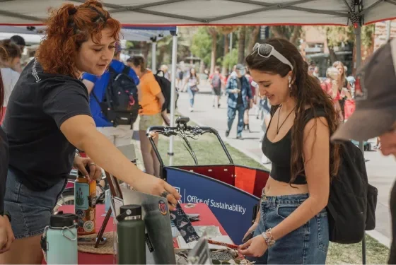 A Campus Sustainability Fund student employee talks with a student at an outdoor tabling event.