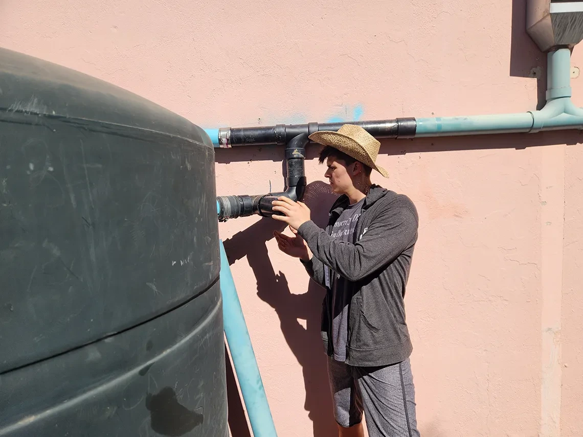 One person is inspecting the pipes that lead to a rainwater cistern.