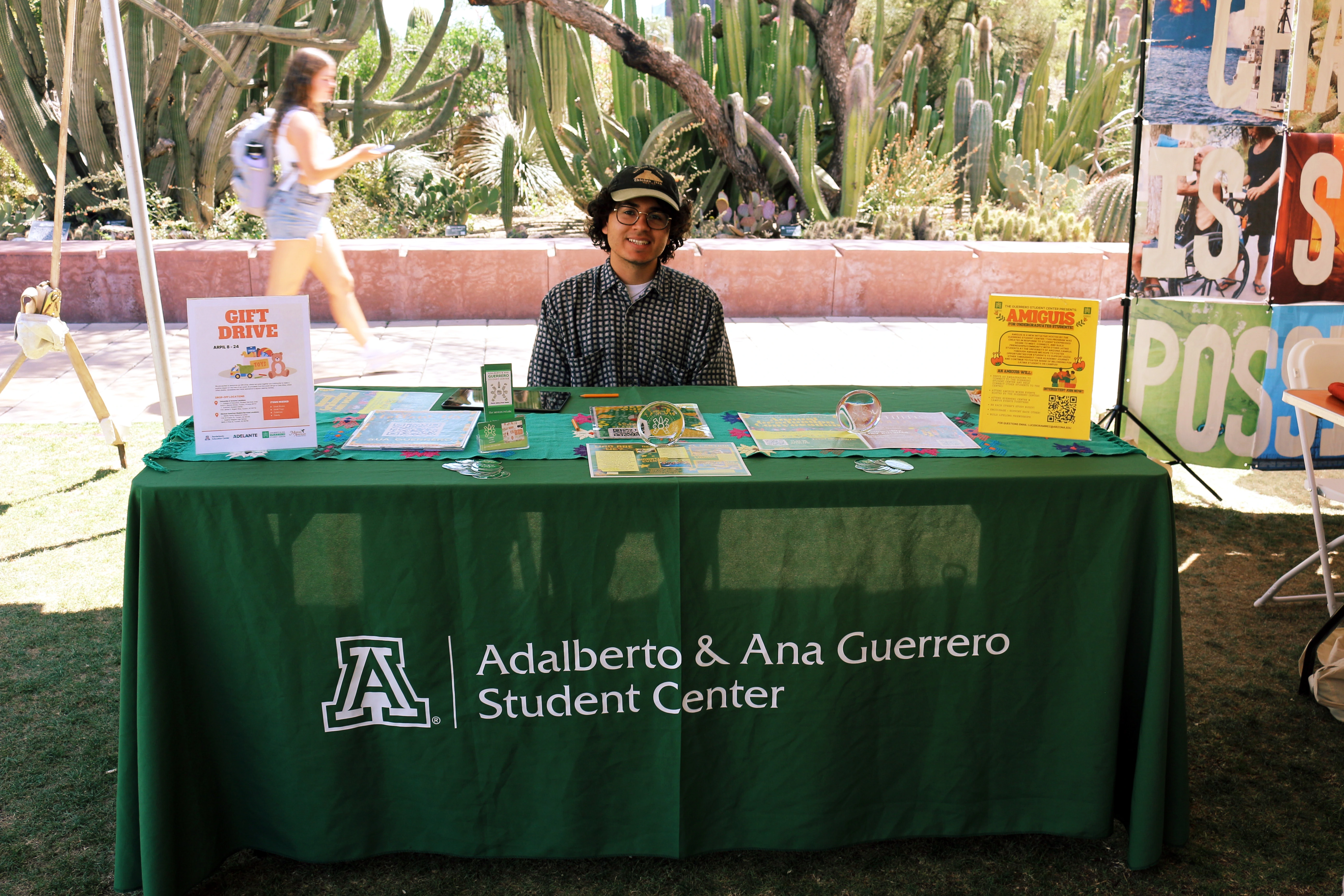 A person smiling and sitting behind a table covered in outreach material.
