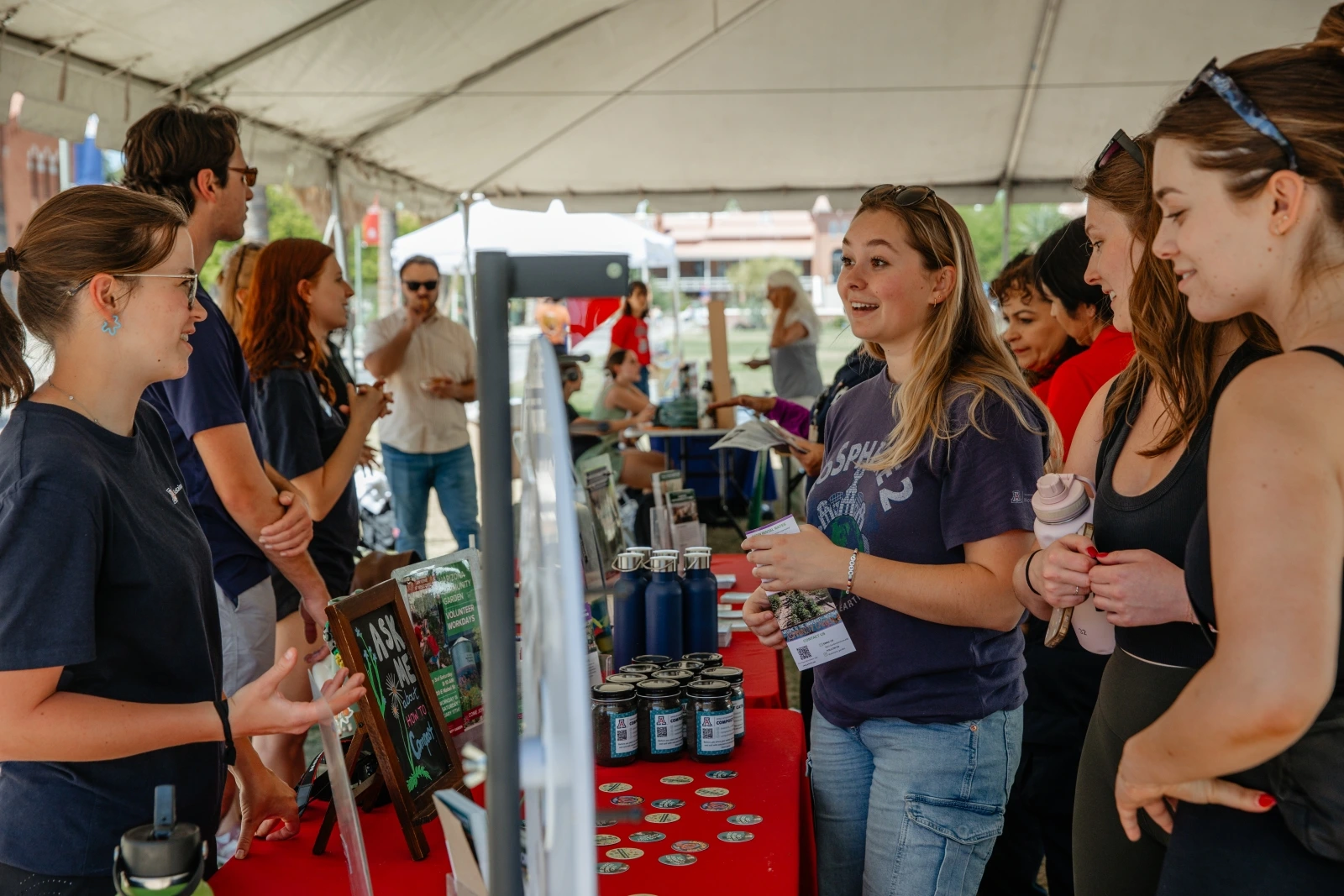 A group of people all talking to one another with a red table in between them. Next to the table is a game wheel that spins.