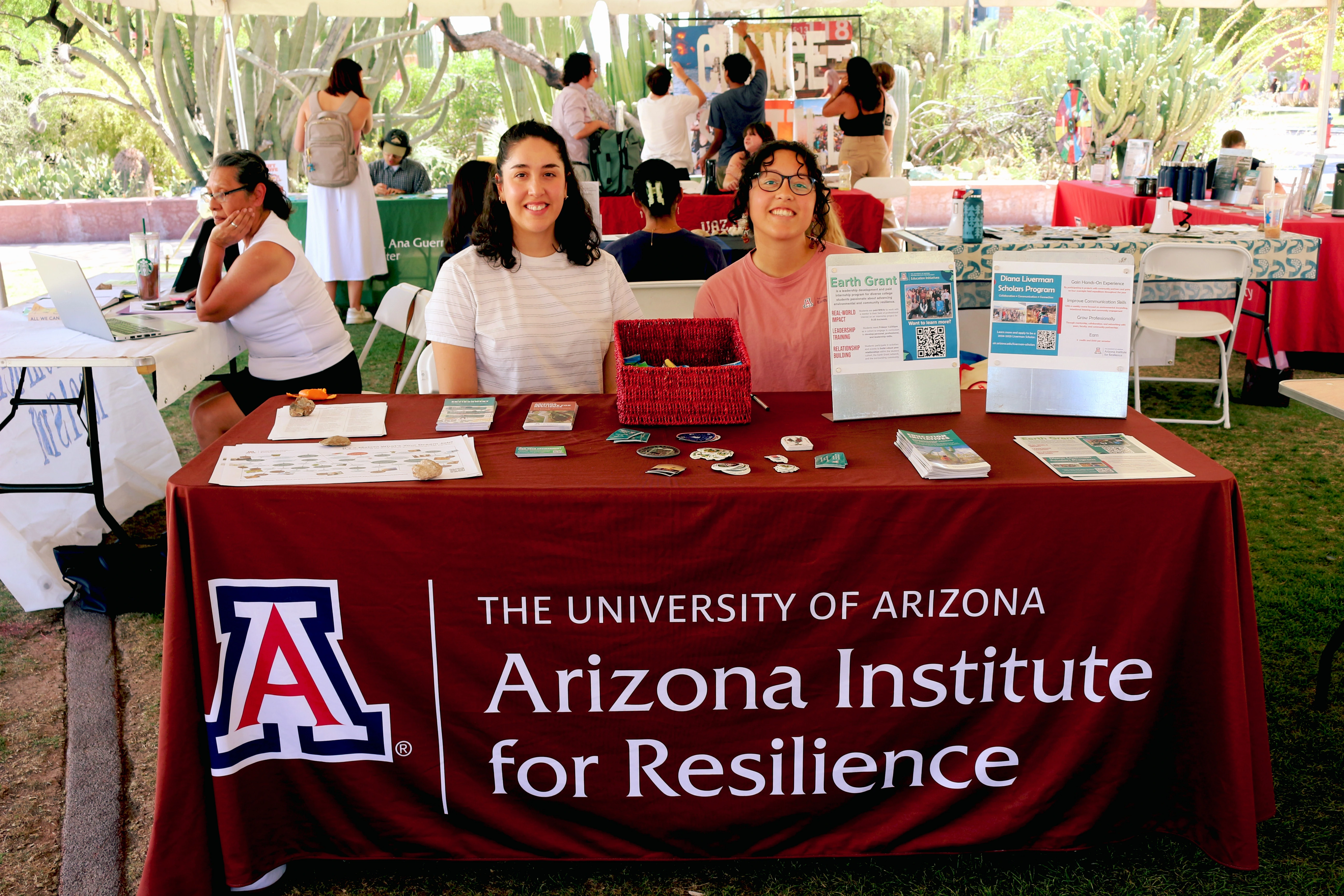 Two people smiling and sitting behind a table covered in outreach material.
