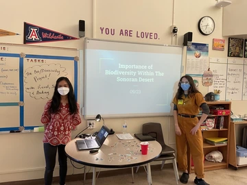 Two classroom educators pose in front of their lesson board. 