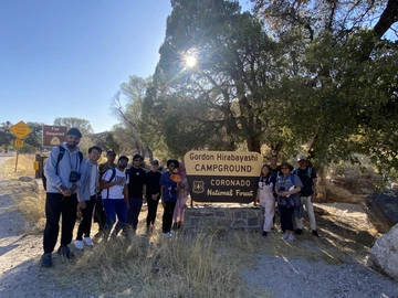 Group of students gathered around the Gordon Hirabayashi Campground sign at Babad Do'ag