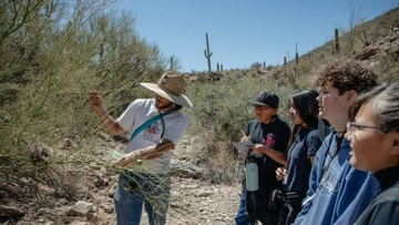 a group of students are gathered around an educator, who is showing them how to identify a desert tree