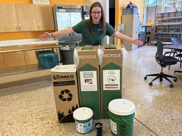 an employee poses with Outdoor Rec's composting and TerraCycle bins, demonstrating how the team is encouraging minimizing their waste!
