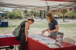 Two people standing on opposite sides of a red table talking to each other at a tabling event.