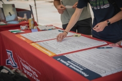 A red table with 3 big posters and a person's hand putting a sticker on the poster.