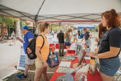 Multiple people standing between red tables talking to each other at a tabling event.