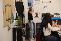 A person standing next to a paper taped on a whiteboard while talking to a group of students.