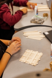 People glueing wooden popsicle sticks together in the shape of a square.