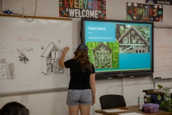 A person writing on a whiteboard that is next to a projector screen.