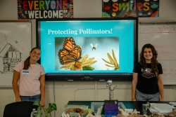 Two people standing on opposite sides of a projector screen smiling.