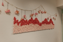 An art installation that is hung on a wall. The two canvases have clay cherry blossoms glued on them. A flower ornament is hanging on top of the installation.