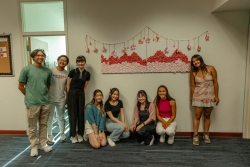 A group of people posing for a photo in front of an art installation that is hung on the wall behind them.