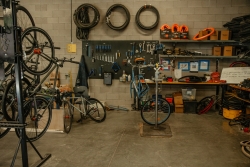 A bike workshop area where tools and wheels are hung on the wall and in storage racks. 