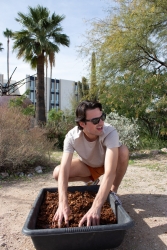 A person squatting down with their hands in a bucket of soil.