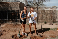 Two people standing next to each other smiling and holding shovels.