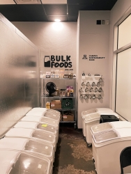 A corner with both side walls lined with bins. The back wall has a storage rack with different jars and items stored on there. One of the walls has a peg board hung up that holds different shaped funnels.