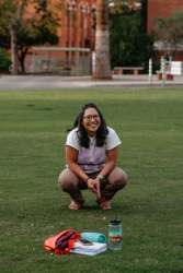 A person squatting down in a grass field talking to a group of people.