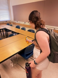 a person standing in a classroom holding a measuring tool to do a lighting audit. 