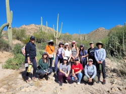 Bio/Diversity cohort visits the desert. The cohort poses in a wash with saguharos behind them.