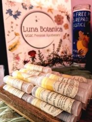 Multiple Apapáchame Tierra desert medicine beeswax sticks displayed on a wooden holder with a sign behind them.