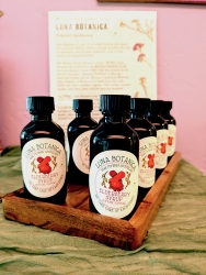 Multiple jars lined up on a wooden holder. The jars contain elderberry syrup.