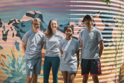 A group of 4 club members pose in front of the mural in the community garden.