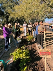 A group of people posing for a photo next to a garden plot.