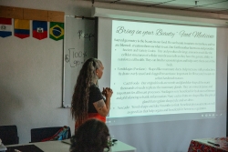 A person standing with both of their hands clasped in front of their chest while they stand next to a projector showcasing a presentation slide.