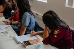 A person sitting and looking down taking notes on a paper.