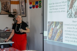 A person holding a cup, smiling, and standing next to a projector that showcases a presentation slide.