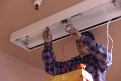 A person on a ladder working on the electrical wires in a light fixture.