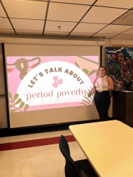 A person standing next to a projector slide starting to present about Period Poverty. 