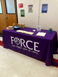 A table covered in a purple cloth with the FORCE logo. On top of the table are various boxes of menstrual cups and wipes. 