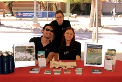 Three people posing for a photo behind a table that is covered in outreach material and a red cloth.