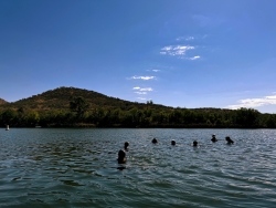 Multiple people submerged in water near a mountain.