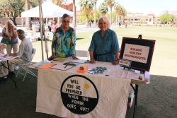 Two people smiling and standing behind a table covered in outreach material.