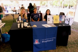 Three people smiling and sitting behind a table covered in outreach material.