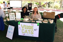 Two people smiling and sitting behind a table covered in outreach material.