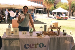 A person smiling and standing behind a table covered in outreach material.