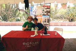 Two people smiling and sitting behind a table covered in outreach material.