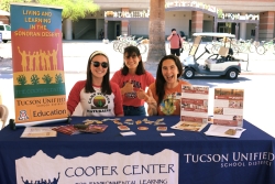 Three people smiling and sitting behind a table covered in outreach material.