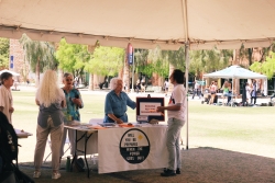 People standing next to a table covered in outreach material. They are talking to the people standing behind the table.