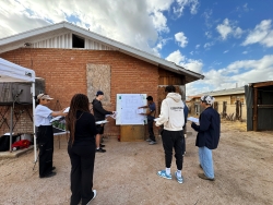 A group of people watching a presentation in front of a house.